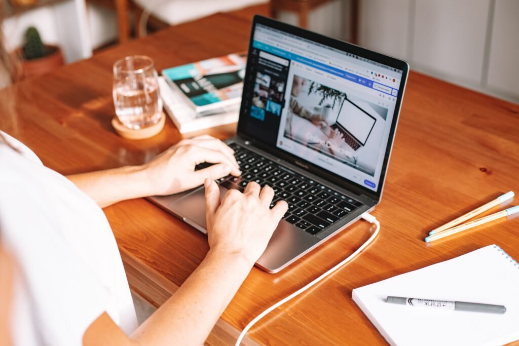 pexels-photo-5912197-5912197 A person working remotely on a laptop at a wooden desk with stationery and a notepad.
