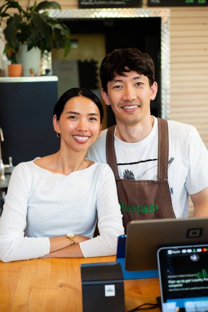 Portrait of two smiling coffee shop owners standing behind counter. Ideal for business and small enterprise themes.